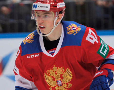 Хоккеист в красной форме сборной России с номером 97 на льду. На свитере герб России, шлем с логотипом Норникель. Игрок внимательно смотрит вперёд, на фоне видно размытое изображение трибун