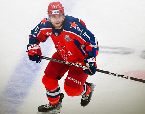 Хоккеист в красной форме с синими и белыми элементами на льду во время игры. На экипировке заметны логотипы и номер 17. Он держит клюшку и активно движется по площадке