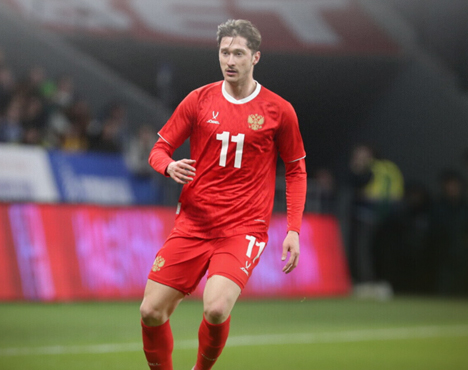 Футболист в красной форме с номером 11 на поле во время матча. На фоне зрители, трибуны и электронное табло